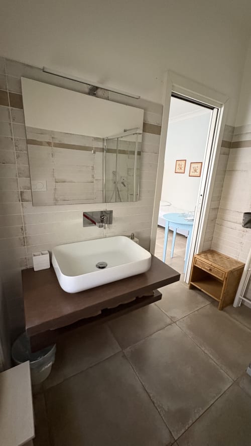 Bagno moderno nella Suite Acquamarina di MAISON TIZI, Roma, con lavabo bianco su top scuro, specchio grande e rivestimenti in piastrelle