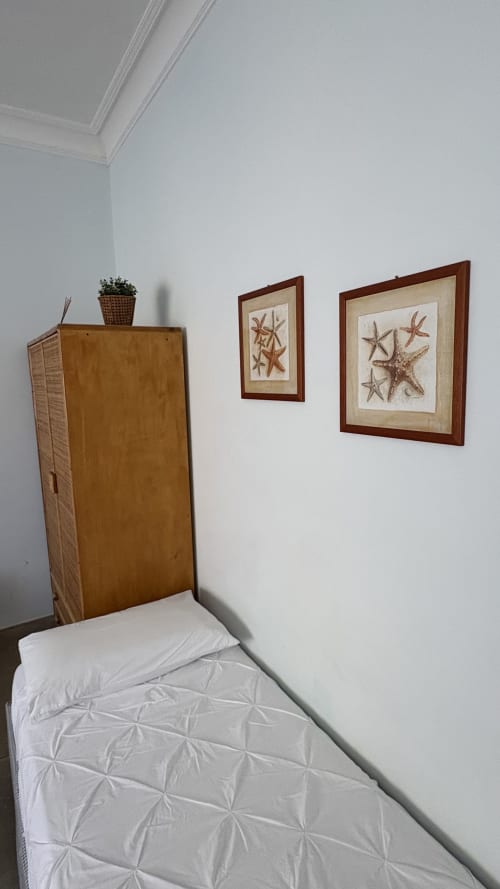 Accogliente angolo camera presso Acquamarina Suite con biancheria bianca, testata in legno, pianta in vaso e decorazioni stelle marine