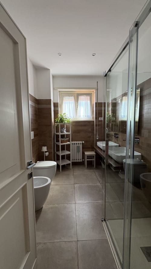 Bagno moderno nella Turchese Suite di MAISON TIZI B&B Roma con doppi lavabi, doccia walk-in e finestra con vista sul giardino