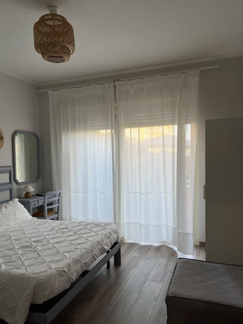 Camera luminosa di Maison Tizi con letto bianco, tende trasparenti, porte con vista sul giardino e lampada a soffitto intrecciata