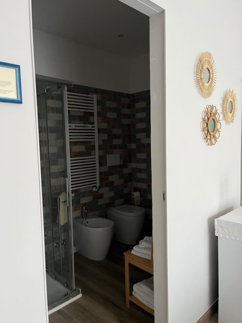 Bagno moderno nella Gardenia Suite di MAISON TIZI con piastrelle nere, WC, bidet, box doccia e asciugamani