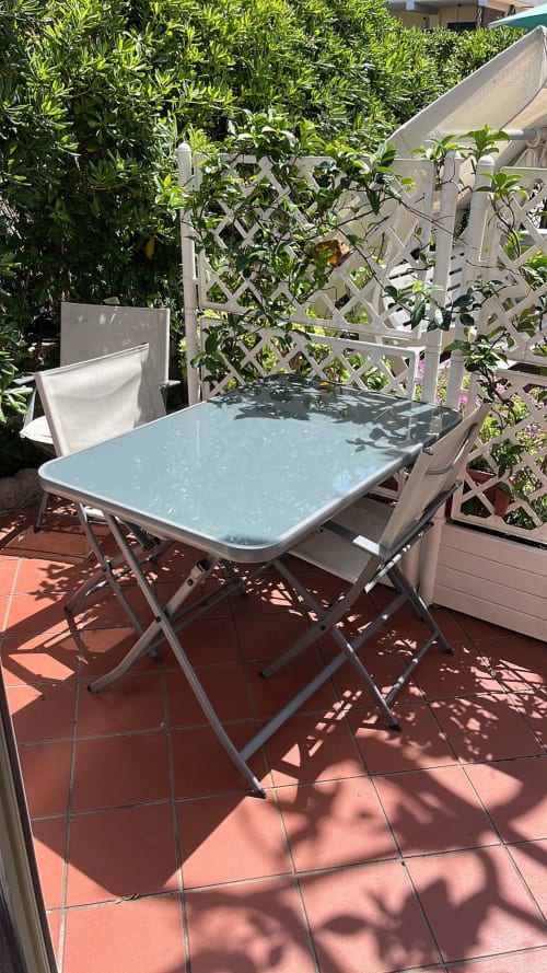 Tavolo da pranzo in patio con superficie azzurra su piastrelle in terracotta, circondato da siepi verdi e schermi a traliccio a Maison Tizi