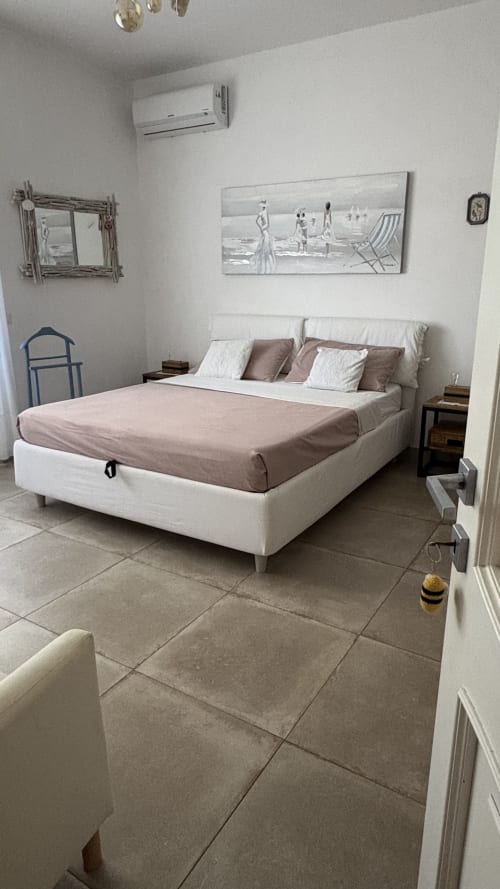 Camera moderna a Maison Tizi con letto bianco, piastrelle beige, opera d'arte, climatizzatore e comodini in Fiumicino Roma