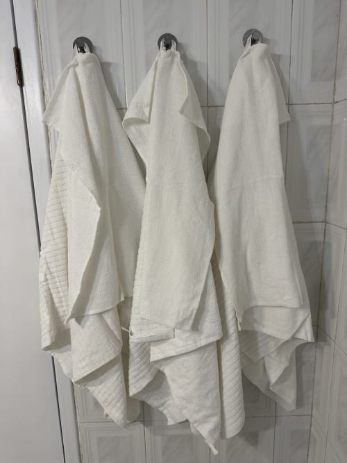 Três toalhas brancas penduradas em ganchos no banheiro do Villas Simone Porto Santo City & Beach Apartments