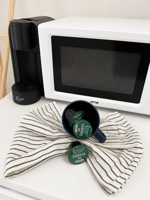Micro-ondas branco com cafeteira preta e cápsulas de café Corposo em pano listrado na Villas Simone Porto Santo