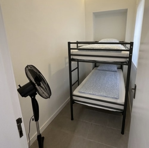 Cama beliche com roupa de cama azul e ventilador preto no quarto compacto da Villas Simone Porto Santo