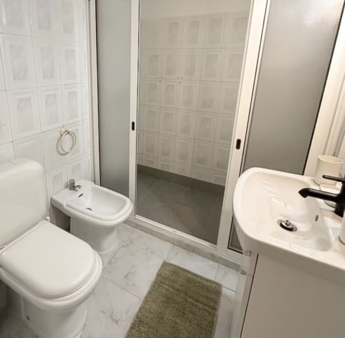 Banheiro moderno em Villas Simone Porto Santo com azulejos brancos, vaso sanitário, bidê, pia e box de vidro