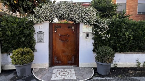 Ingresso di Maison Tizi con porta in legno, muri bianchi, rampicanti fioriti e piante in vaso a Passoscuro Fiumicino Roma