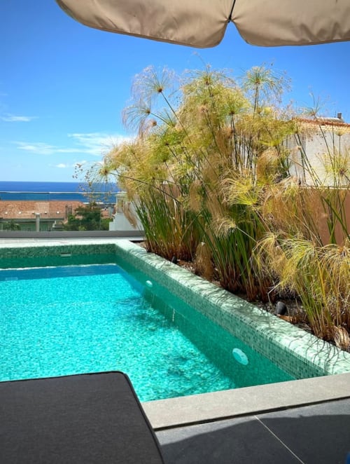Piscina azul-turquesa com guarda-sol bege e plantas ornamentais nas Villas Simone, com vista para o oceano em Portugal