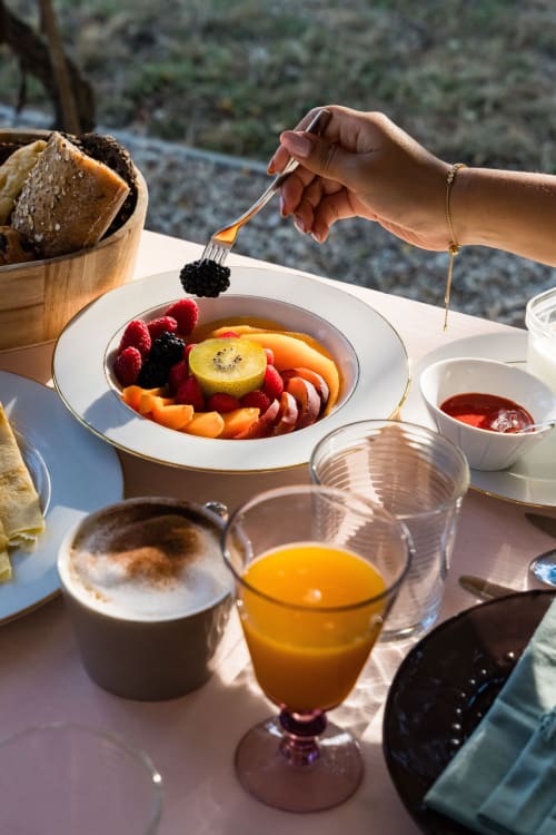 Petit-déjeuner élégant au Domaine de la Peyrine : assiette de fruits frais, baies, jus d'orange et pain artisanal avec vue