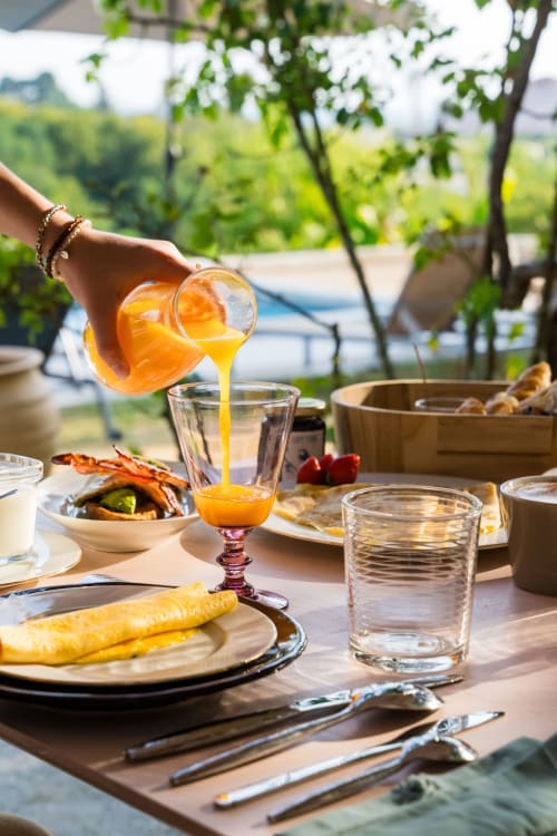 Du jus d'orange frais versé à la table du petit-déjeuner en plein air avec vue sur la campagne au Domaine de la Peyrine, Carignan de