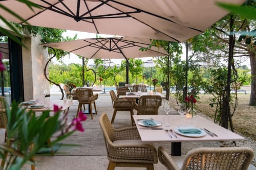 Terrasse de restauration extérieure au Domaine de la Peyrine avec chaises en osier, parasols et vue sur les vignobles de Carignan de Bordeaux