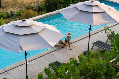 Femme se relaxant près d'une piscine cristalline sous des parasols blancs à l'hôtel Domaine de la Peyrine à Bordeaux