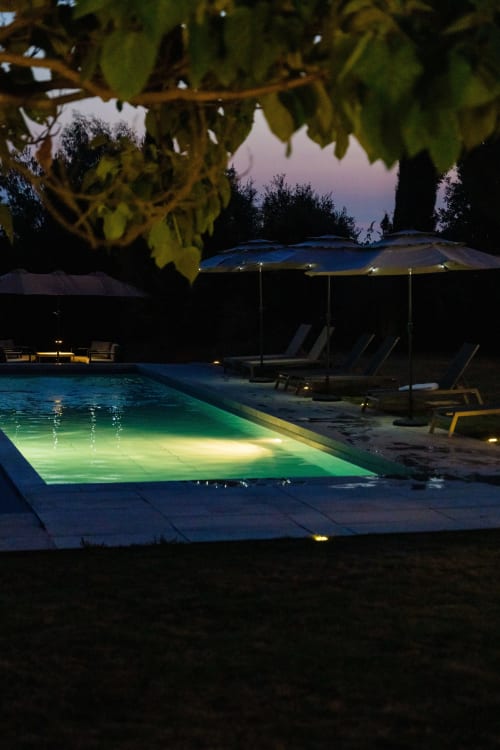 Piscine illuminée du Domaine de la Peyrine à Carignan de Bordeaux, avec transats et parasol bleu au crépuscule