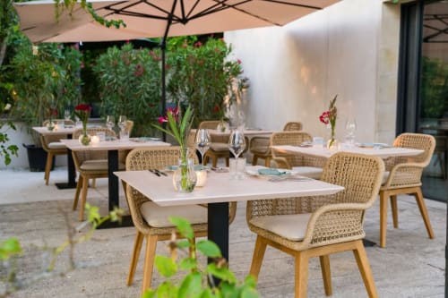 Élégante terrasse de restauration extérieure au Domaine de la Peyrine avec chaises tissées, tables blanches et verdure luxuriante à Carignan de