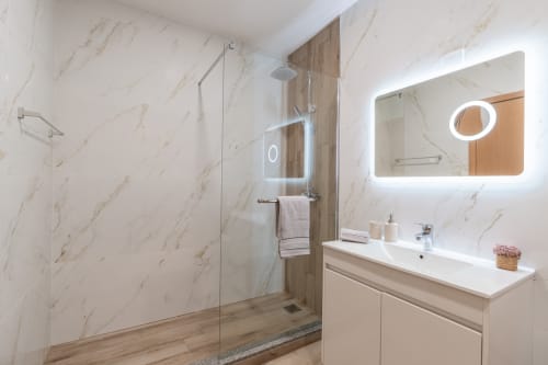 Modern bathroom with marble walls, glass shower enclosure, white vanity with sink, and illuminated mirror at Garry's Holiday