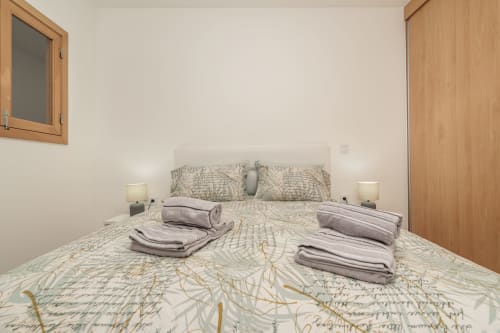 Bright bedroom with map-patterned bedding, gray pillows, folded towels, side lamps, wooden doors and window at Michaels