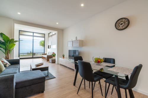 Modern apartment living and dining area at Michaels Garden with ocean view balcony, black chairs, sofa, and kitchen access in