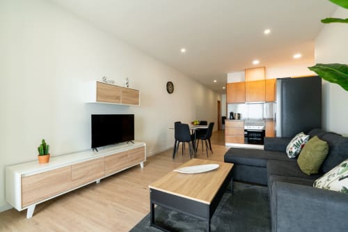Modern open-plan apartment living area at Michaels Garden with dark sofa, wooden TV unit, kitchenette, and dining table at