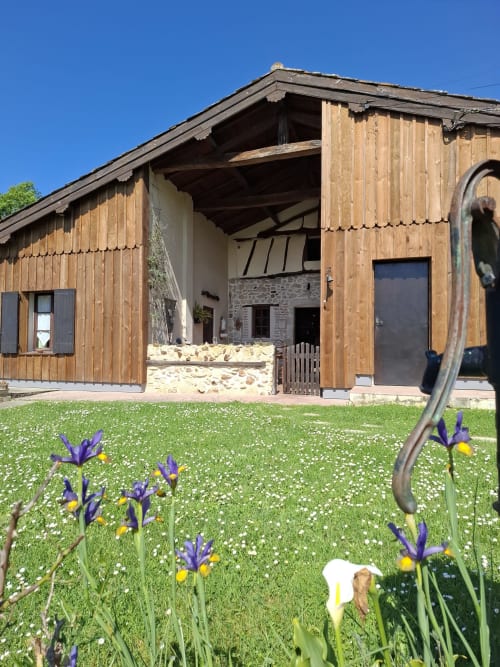 Les Gravets guesthouse in Sigalens with wooden exterior, stone courtyard, blooming iris garden, and clear blue sky