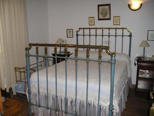 Cama de hierro vintage con barras de latón en habitación estándar del Hotel Plaza Chica, Cartaya, con ropa de cama blanca y decoración de época
