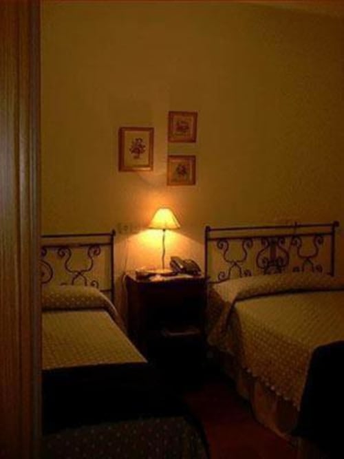 Acogedora habitación doble del Hotel Plaza Chica con camas gemelas, lámpara de mesita y cuadros en pared amarillo mostaza