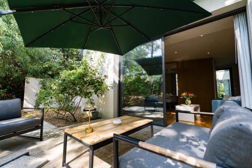 Terrasse de jardin du Domaine de la Peyrine avec parasol vert, mobilier contemporain et portes vitrées menant à la Suite Robin.