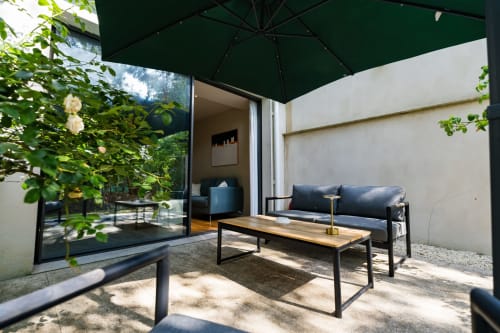 Terrasse de la Suite Robin à la Domaine de la Peyrine avec vue sur le jardin, canapé, table et parasol vert