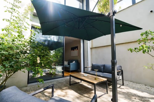 Terrasse moderne du Domaine de la Peyrine avec parasol en porte-à-faux noir, table en bois et sièges sombres donnant sur le jardin