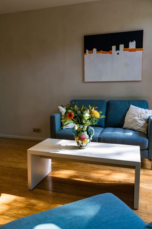 Élégant salon contemporain au Domaine de la Peyrine avec canapé bleu, table basse blanche, fleurs fraîches et tableau urbain abstrait