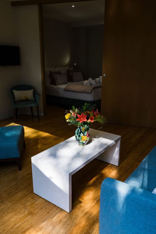 Suite Robin au Domaine de la Peyrine avec table basse blanche, fleurs colorées, chaises bleues et vue sur la chambre