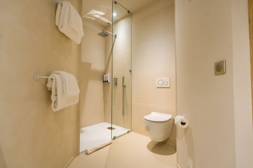 Salle de bains moderne avec douche vitrée, toilettes murales et porte-serviettes à l'hôtel Domaine de la Peyrine à Bordeaux