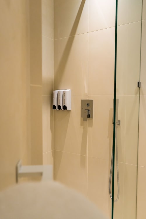 Douche moderne de l'hôtel Domaine de la Peyrine avec carrelage beige, distributeurs de savon et accessoires chromés