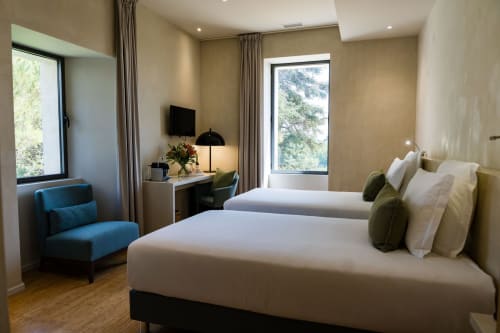 Chambre d'hôtel moderne avec deux lits, fauteuil bleu, bureau avec TV et vue sur le jardin au Domaine de la Peyrine, Bordeaux