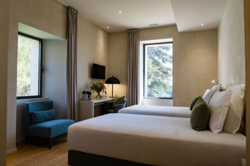 Chambre spacieuse au Domaine de la Peyrine avec lits jumeaux, fauteuil bleu, bureau et vue sur le jardin par grandes fenêtres