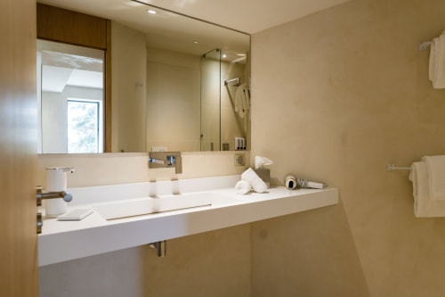 Salle de bain moderne de la Chambre Huppe du Domaine de la Peyrine avec lavabo blanc, miroir et douche aux tons neutres chaleureux.