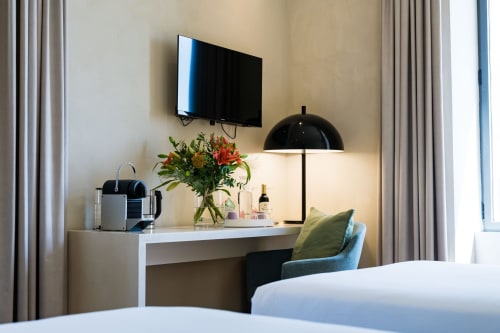 Bureau moderne de chambre d'hôtel à Domaine de la Peyrine avec TV, fleurs fraîches, lampe et fauteuil confortable à Carignan de Bordeaux