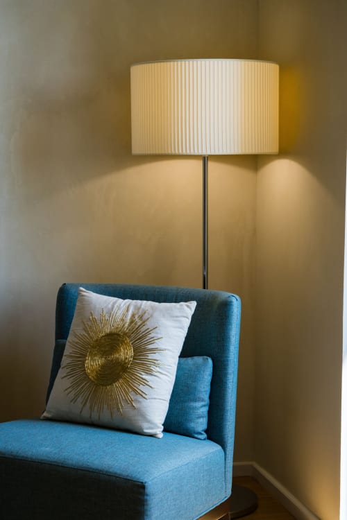 Coin moderne d'une suite hôtelière avec fauteuil bleu-vert, coussin soleil doré et lampadaire contemporain à abat-jour plissé blanc au Domaine