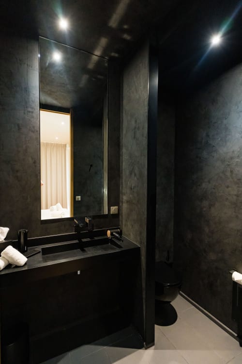 Salle de bains contemporaine de la Suite Hirondelle au Domaine de la Peyrine avec murs en pierre noire, miroir rétroéclairé et accessoires noirs