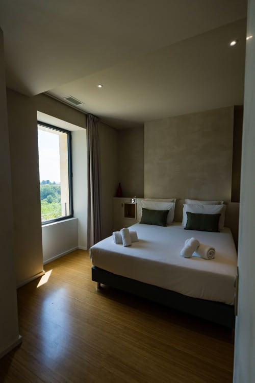 Chambre moderne du Domaine de la Peyrine avec vue sur le jardin, literie blanche, parquet et lumière naturelle de la baie vitrée