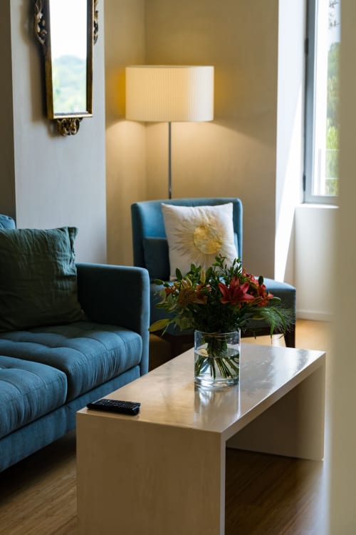 Salon moderne de la Suite Hirondelle au Domaine de la Peyrine avec canapé bleu, fleurs fraîches et vue sur le jardin