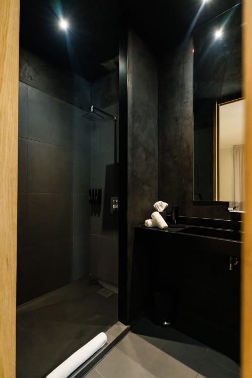 Salle de bains luxe moderne dans la Suite Hirondelle du Domaine de la Peyrine avec douche carrelage noir, vasque, serviettes blanches et ambiance