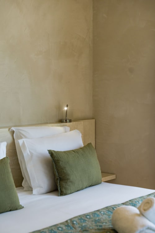 Chambre Pinson Suite au Domaine de la Peyrine avec oreillers blancs, coussins verts et murs beige minimaliste à Carignan de