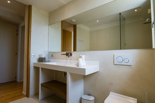 Salle de bains moderne de la Suite Pinson au Domaine de la Peyrine avec lavabo flottant blanc, grand miroir et douche à l'italienne