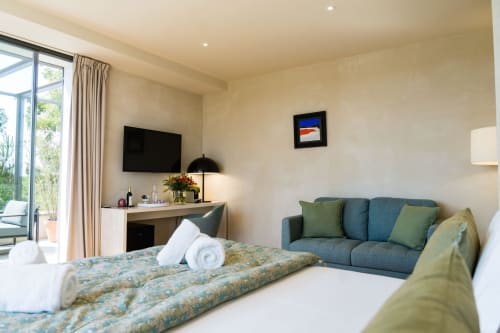 Suite Pinson au Domaine de la Peyrine avec lit, canapé bleu, bureau avec TV et balcon vue jardin