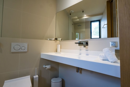 Salle de bains moderne de la Suite Tourterelle au Domaine de la Peyrine avec vasque blanche, grand miroir et équipements contemporains