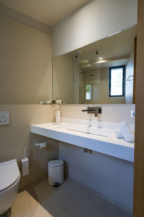 Salle de bains moderne de la Suite Tourterelle au Domaine de la Peyrine avec lavabo blanc, miroir et carrelage foncé