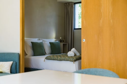 Chambre Tourterelle au Domaine de la Peyrine avec lit blanc, coussins verts et vue sur le jardin par la fenêtre