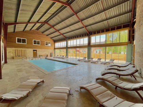 Piscine intérieure du Domaine Les Racines avec transats et grandes baies vitrées donnant sur Croix-Moligneaux