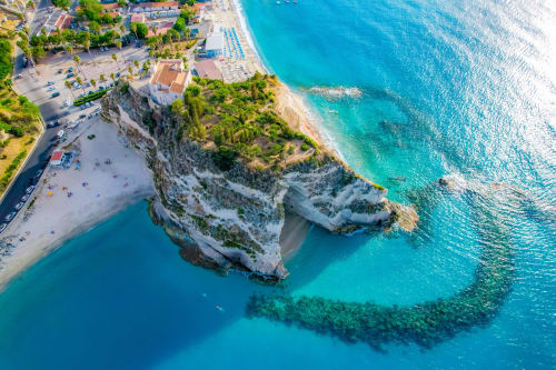 Vista aerea delle spettacolari scogliere bianche di Tropea, acque turchesi e spiaggia sabbiosa con bagnanti presso Mottola